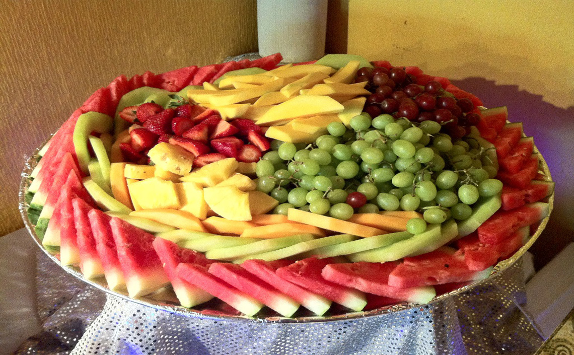 A large platter arranged with watermelon, sliced fruit, grapes, and berries.