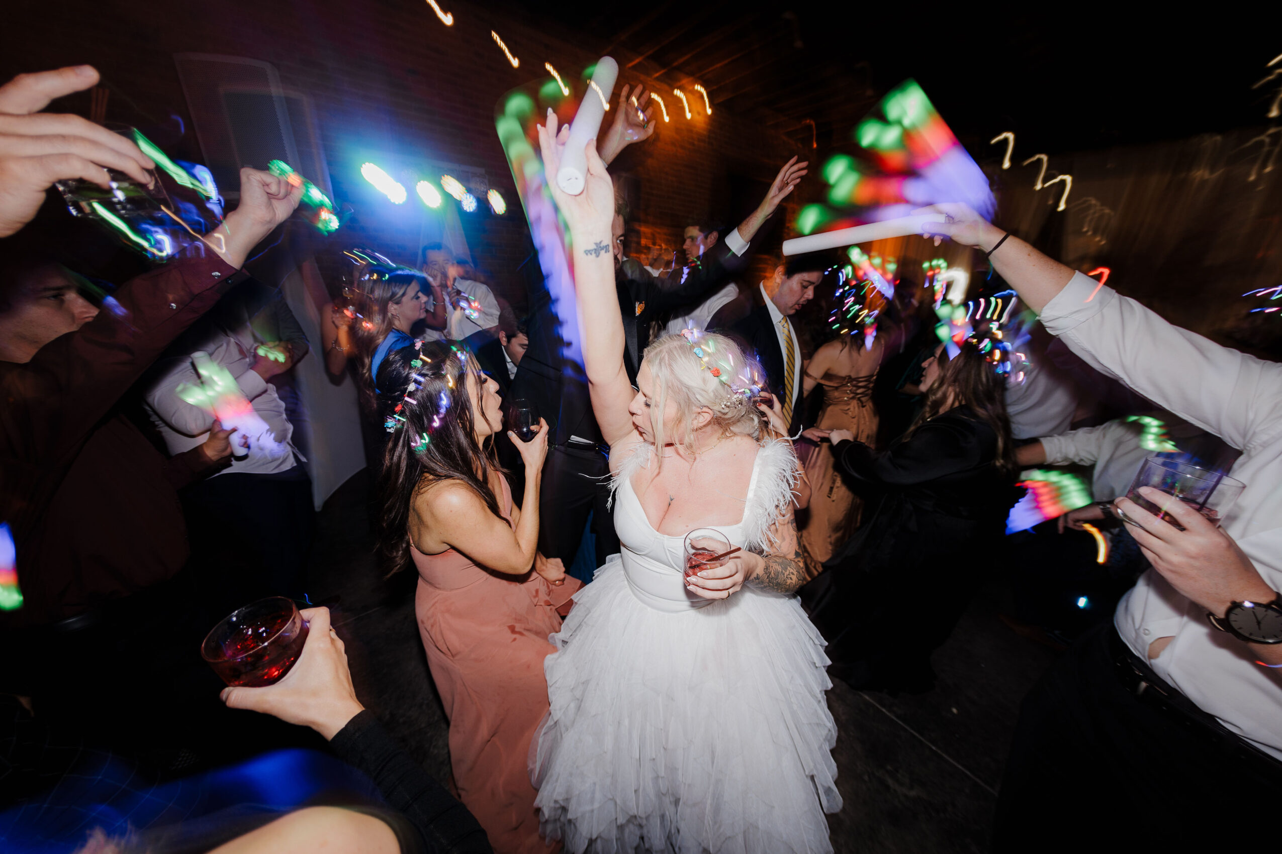 A person in a white dress dances amid a crowd holding glowing lights and phones.