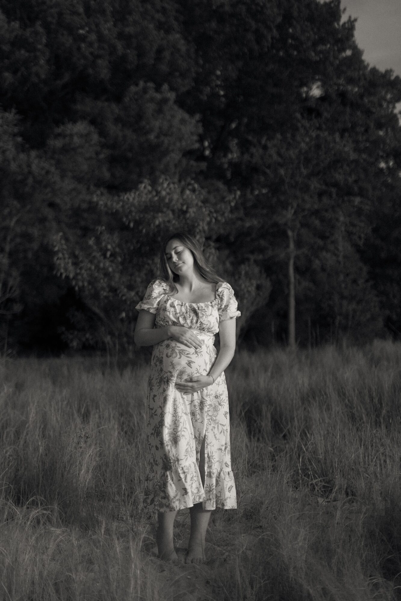 A person in a patterned dress stands in tall grass with trees behind them.