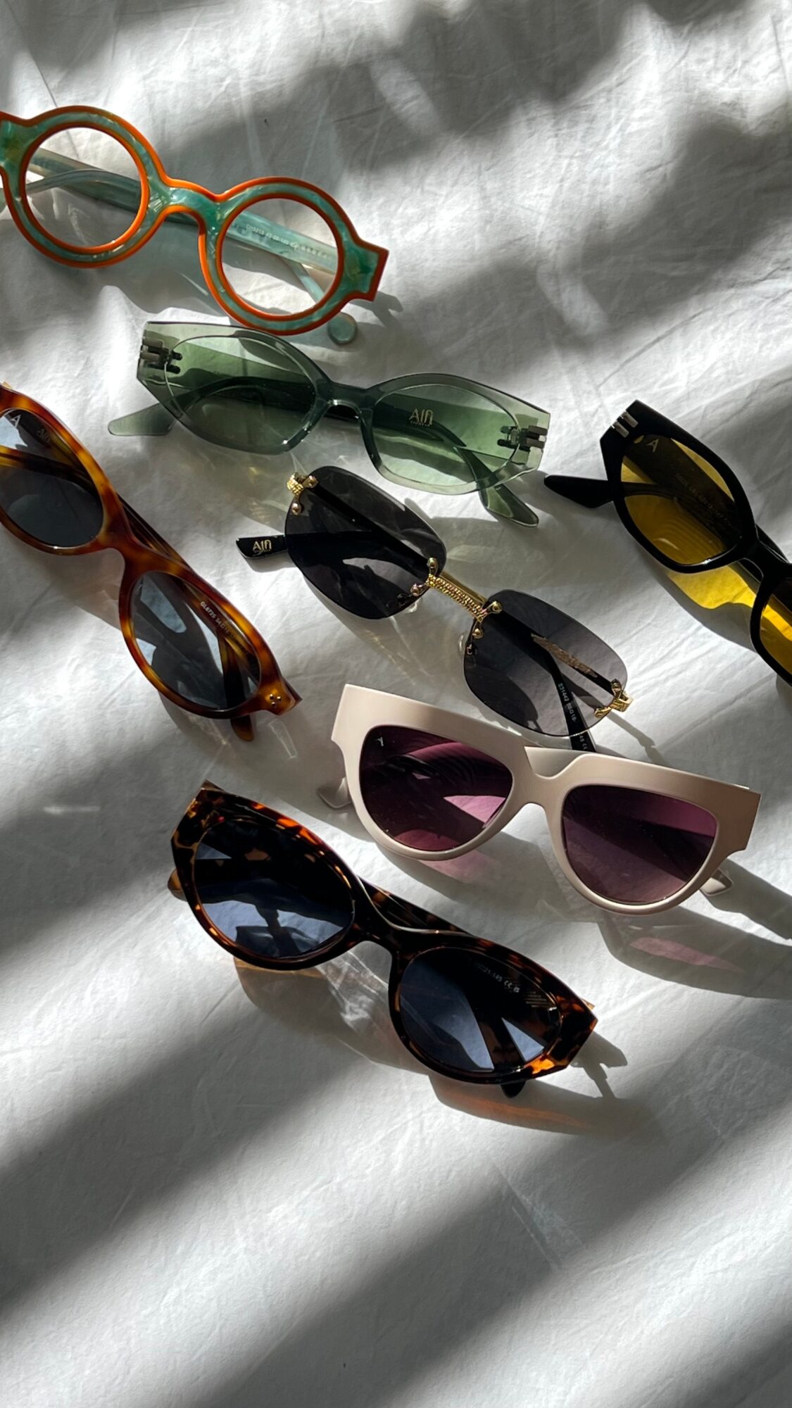 Several pairs of sunglasses arranged on a white surface in strong sunlight.