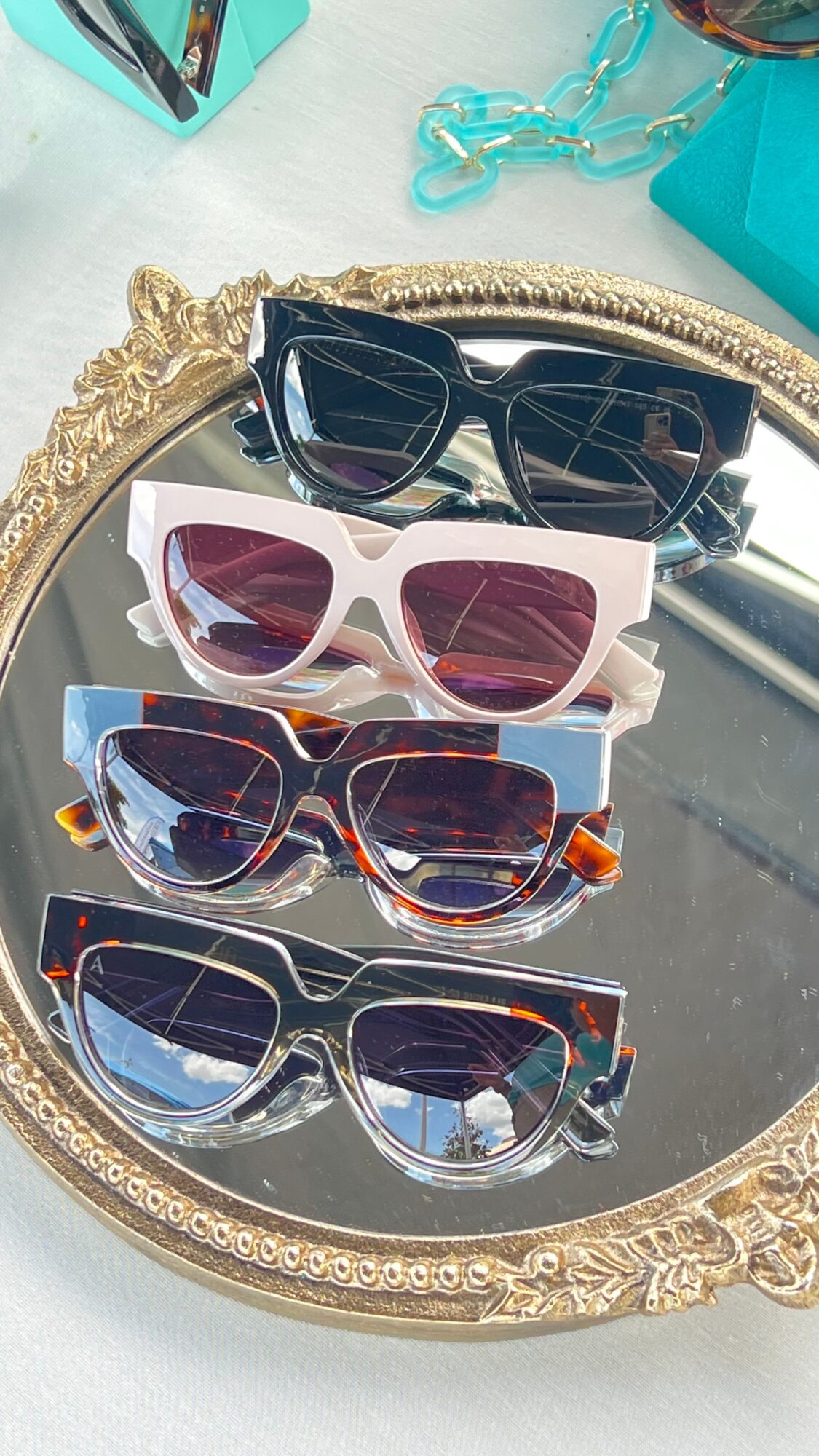 Four pairs of sunglasses arranged on an ornate oval mirror.