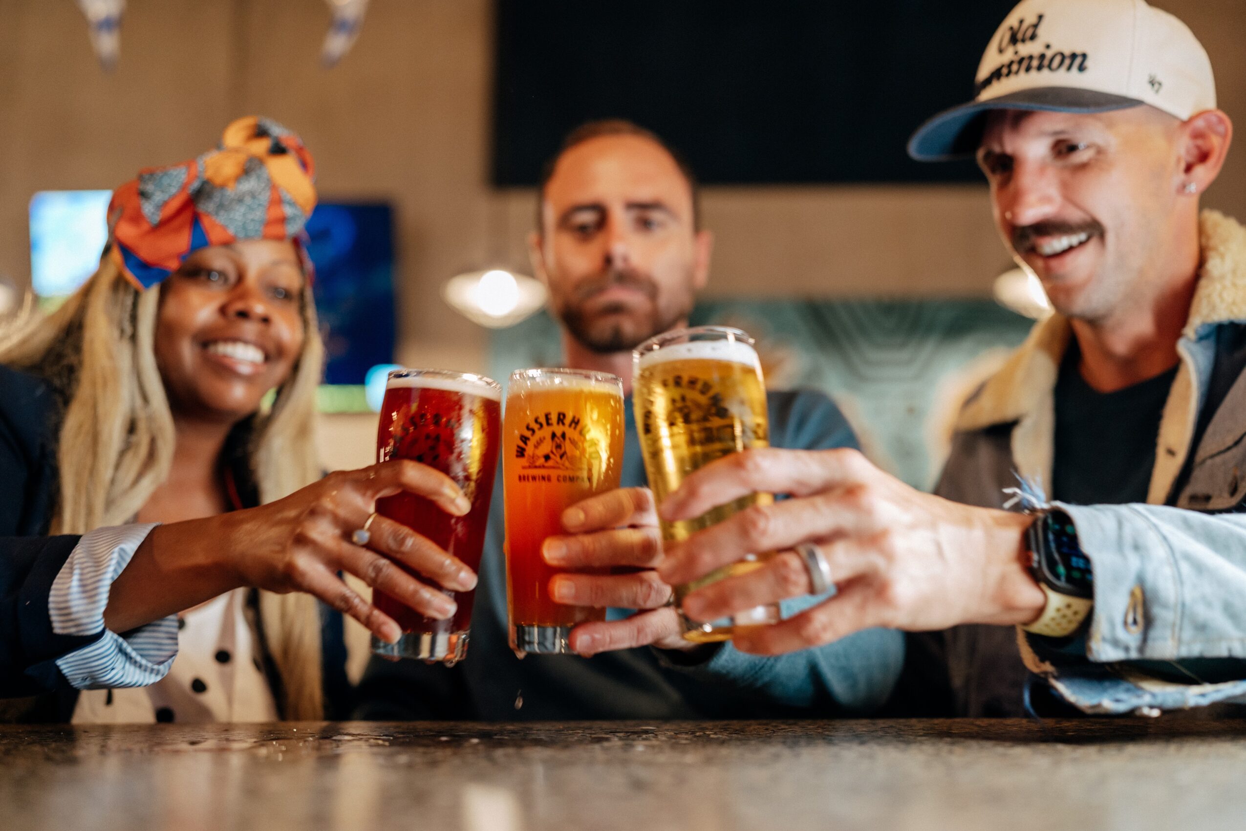 Three people clink glasses of beer at a bar.