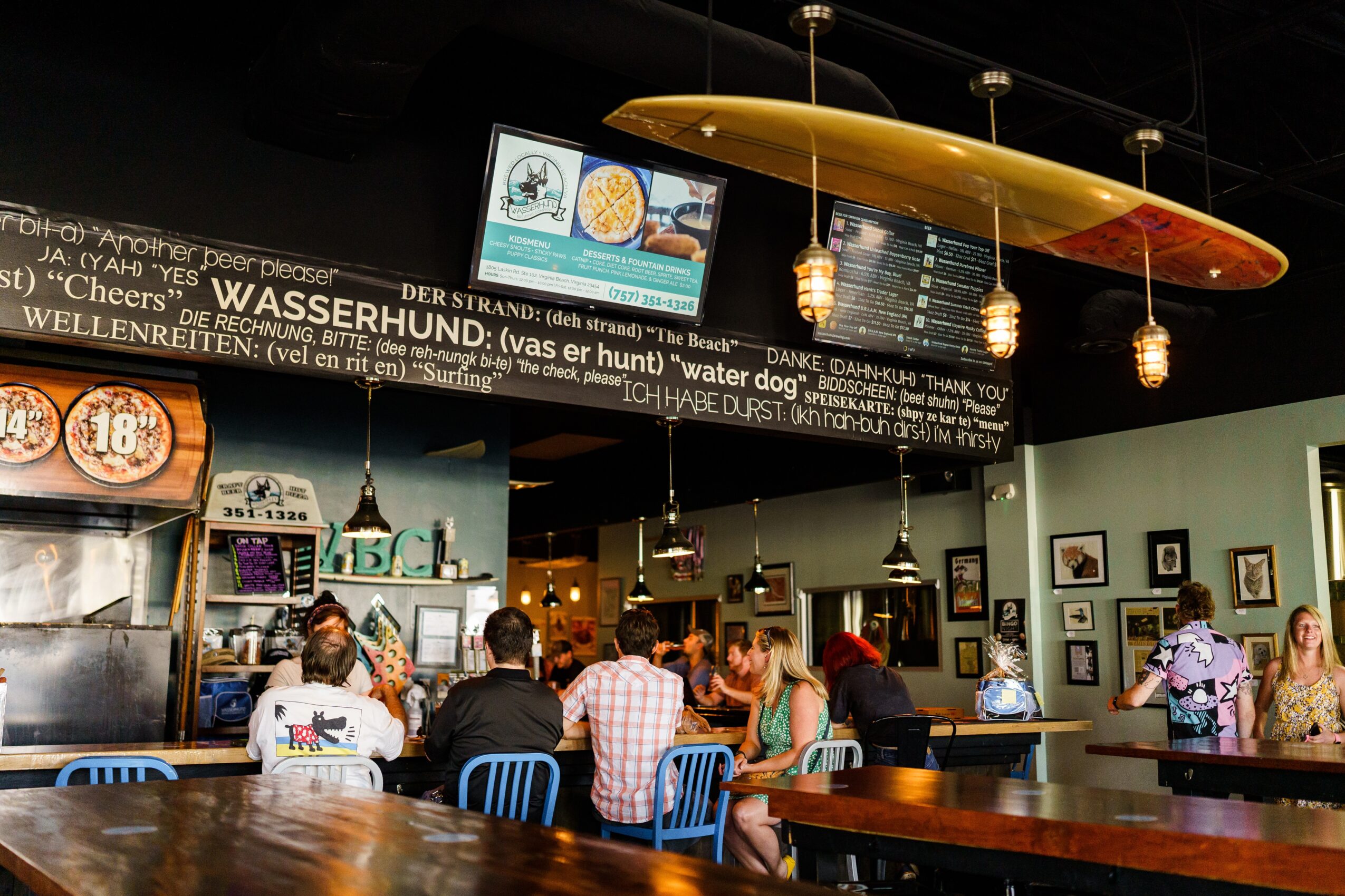 People seated at a restaurant counter beneath a long hanging yellow canoe, with menu boards and pendant lights.