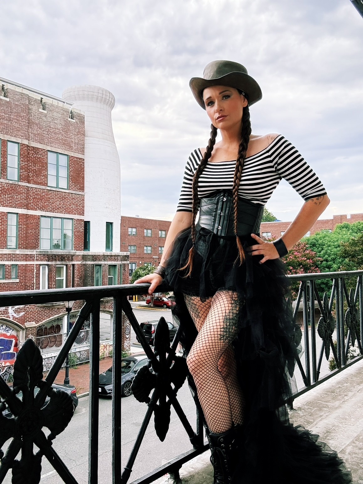 Person in a black hat and striped shirt standing on a balcony beside a metal railing.