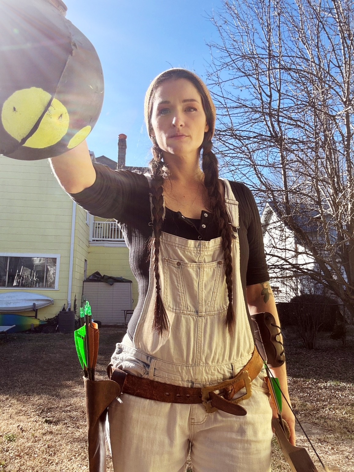 Person in a white outfit holding a large paddle toward the camera, with a house and leafless trees behind them.