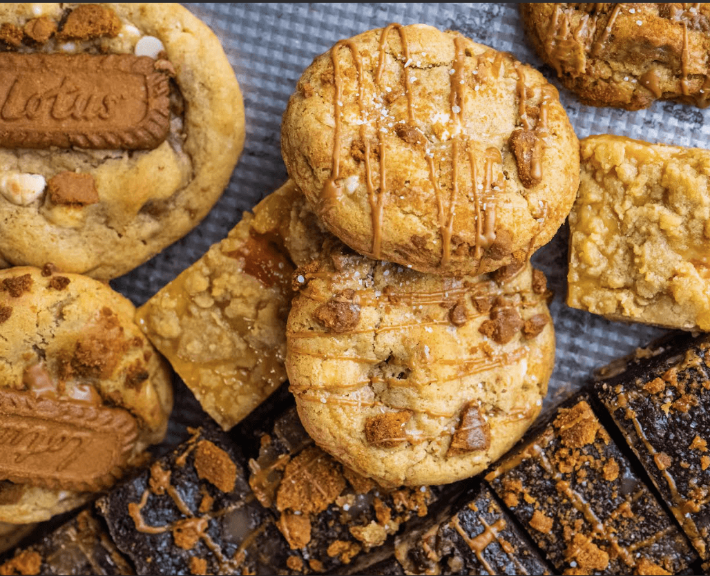 Assorted cookies and bars arranged closely together, including round cookies topped with chocolate pieces and rectangular baked bars.