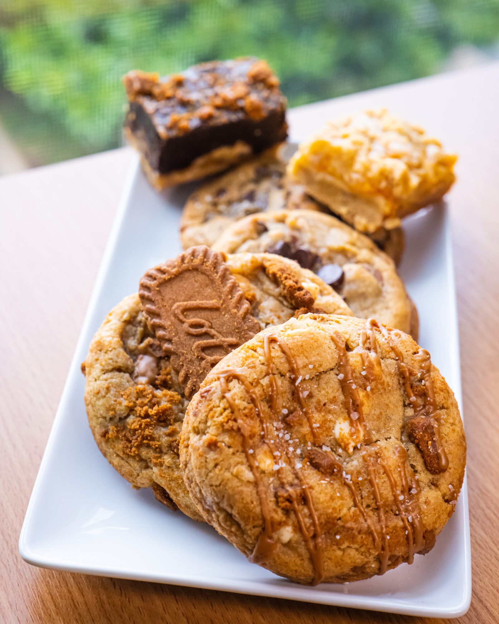 A white plate holds assorted cookies and square pastries on a table.